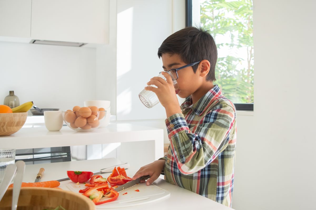 A child drinking a glass of clean filtered water in the kitchen, peace of mind for the family